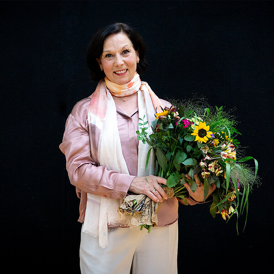 Christine Camillo mit Blumenstrauß vor schwarzem Hintergrund