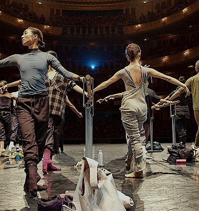 Tänzer*innen an der Stange auf der Bühne der Staatsoper Unter den Linden. Im Hintergrund das beleuchtete Auditorium.