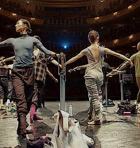 Tänzer*innen an der Stange auf der Bühne der Staatsoper Unter den Linden. Im Hintergrund das beleuchtete Auditorium.